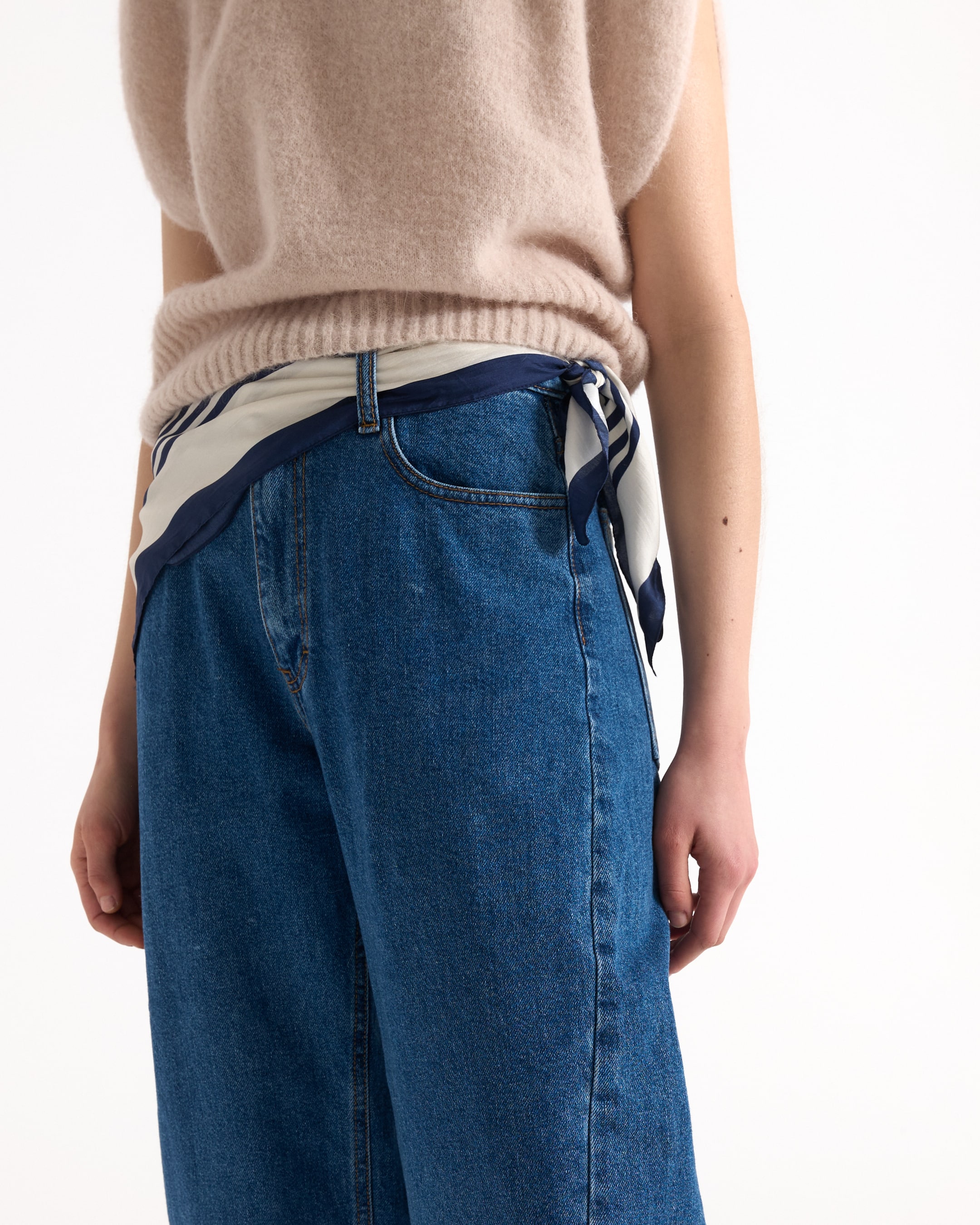 draagt blauwe spijkerbroek, blauw denim, hoog taille, sjaalriem, breisels sweater